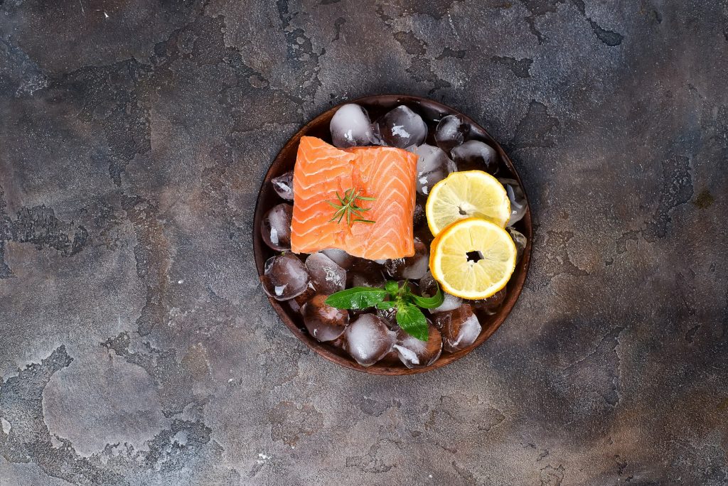 Salmon steaks on ice with lemon slice on wooden plate. Lean proteins.