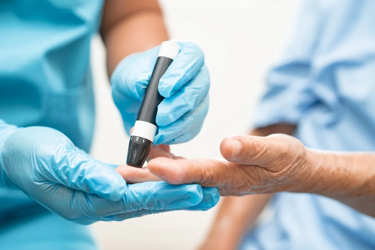 Análisis de Sangre en Tamarac: Qué Exámenes Necesita Cada Año Después de los 60 2 Manos con guantes realizan una prueba de glucosa con lanceta en el dedo de una persona mayor