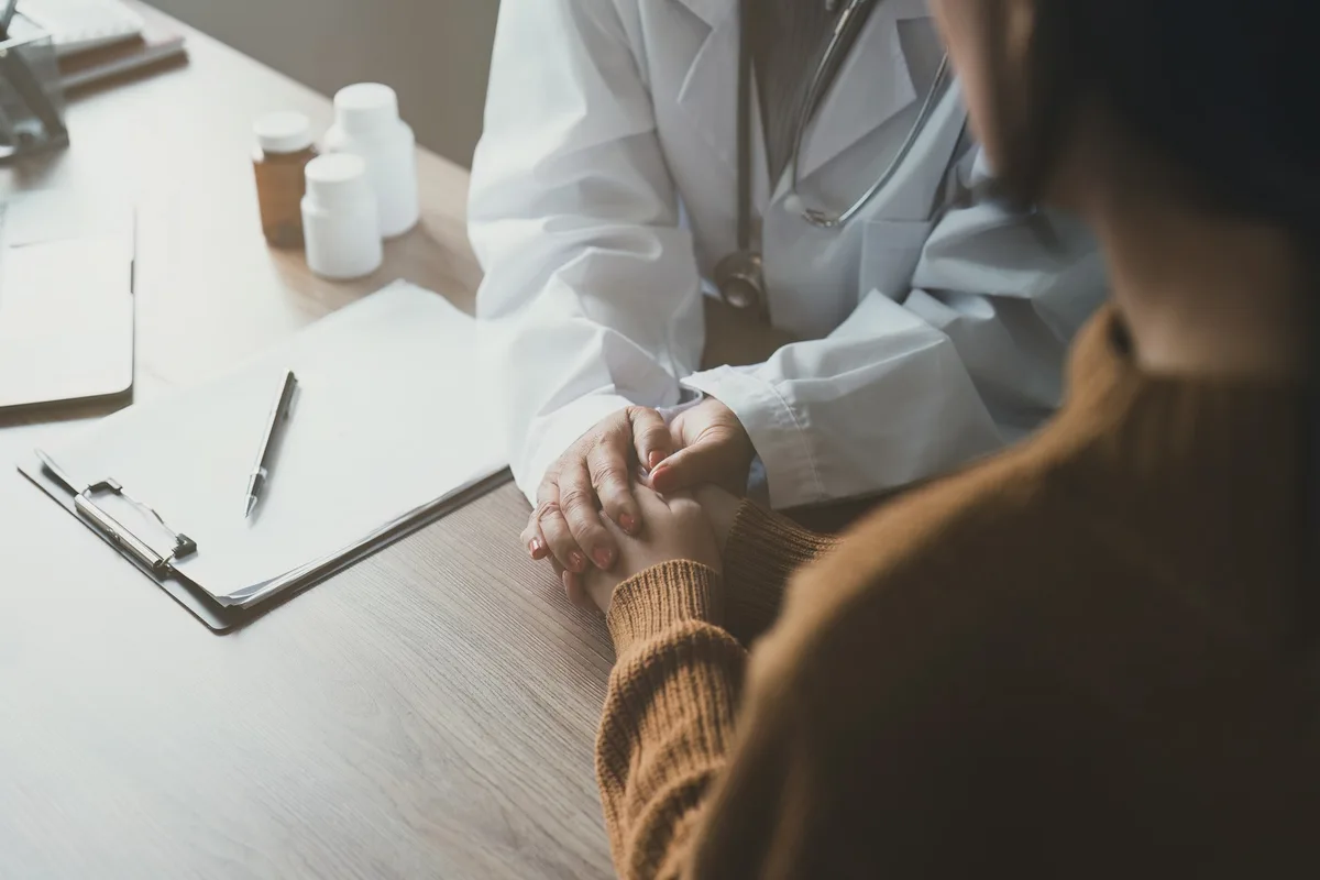 Análisis de Sangre en Tamarac: Qué Exámenes Necesita Cada Año Después de los 60 3 Una profesional de la salud sostiene las manos de una paciente mayor sobre un escritorio con documentos y frascos de medicamento